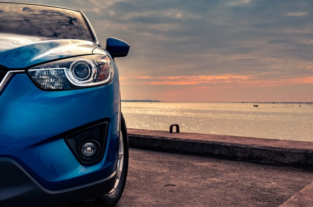 Ein blauer, kompakter SUV im sportlichen und modernen Design, der bei Sonnenuntergang am Abend auf einer Betonstraße am Meer geparkt ist. Konzept für Hybrid- und Elektrofahrzeugtechnologie. Parkplatz. Automobilindustrie.